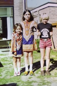 Caz and her siblings standing on a lawn in front of their childhood home, captured from an 8mm film.