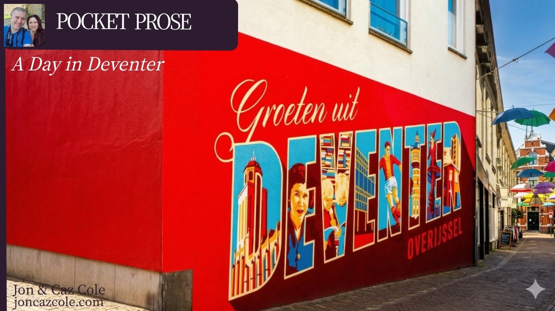A vibrant red street mural in Deventer, Netherlands, featuring the town's name in illustrated letters, with colorful umbrellas hanging over a medieval cobblestone alleyway